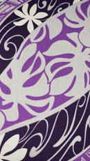 "A close-up video showcasing the 'Tiare Monstera' fabric, featuring a vibrant purple and dark navy wave-print background. The design is layered with white Tiare (gardenia) flowers and purple Monstera leaves, accented by intricate white traditional Polynesian tattoo-style geometric patterns. The video pans across the textile to show the repeating motif and the slight texture of the poly-cotton blend."